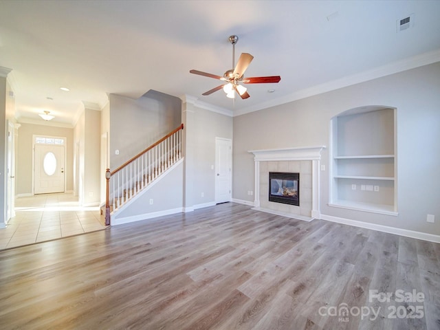 unfurnished living room with built in shelves, a tiled fireplace, light hardwood / wood-style flooring, and ornamental molding