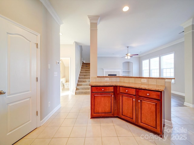 kitchen featuring crown molding, ceiling fan, light stone countertops, light tile patterned flooring, and decorative columns