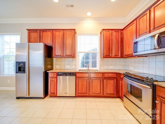 kitchen with sink, ornamental molding, backsplash, stainless steel appliances, and light stone counters