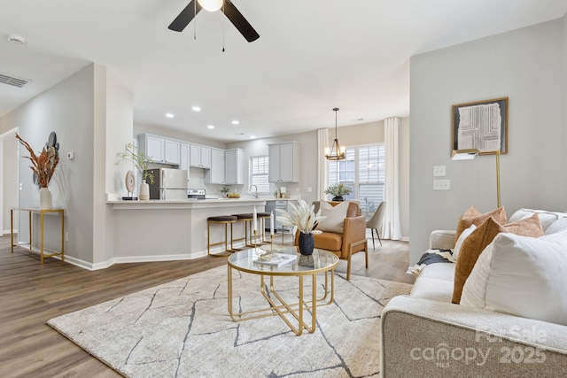 living room with ceiling fan with notable chandelier and light hardwood / wood-style floors