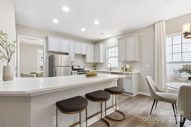 kitchen featuring a kitchen bar, hardwood / wood-style flooring, stainless steel appliances, light stone countertops, and white cabinets