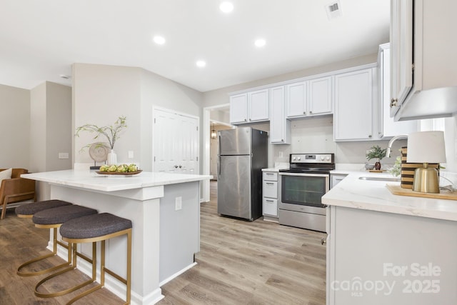 kitchen featuring sink, light wood-type flooring, stainless steel appliances, light stone countertops, and white cabinets