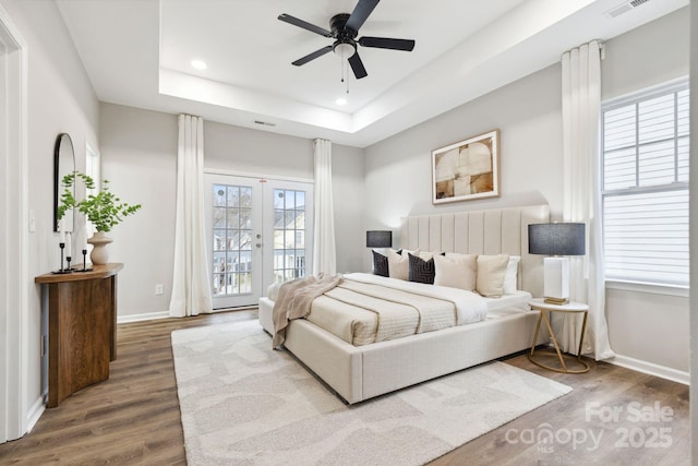 bedroom with wood-type flooring, access to exterior, ceiling fan, a raised ceiling, and french doors