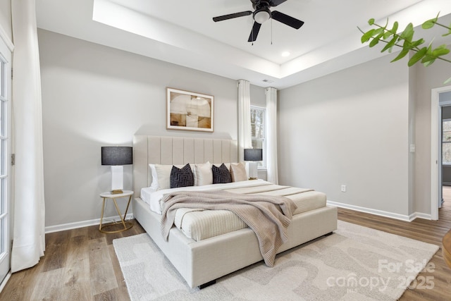 bedroom with ceiling fan, a raised ceiling, and hardwood / wood-style floors