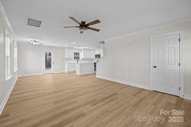 unfurnished living room with sink, ornamental molding, ceiling fan, and light wood-type flooring