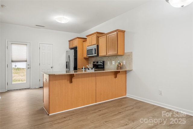 kitchen with decorative backsplash, a kitchen breakfast bar, kitchen peninsula, and stainless steel appliances