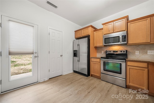 kitchen featuring decorative backsplash, light hardwood / wood-style flooring, light stone counters, and appliances with stainless steel finishes