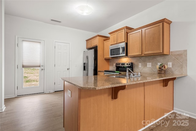 kitchen featuring kitchen peninsula, decorative backsplash, stainless steel appliances, and light hardwood / wood-style floors