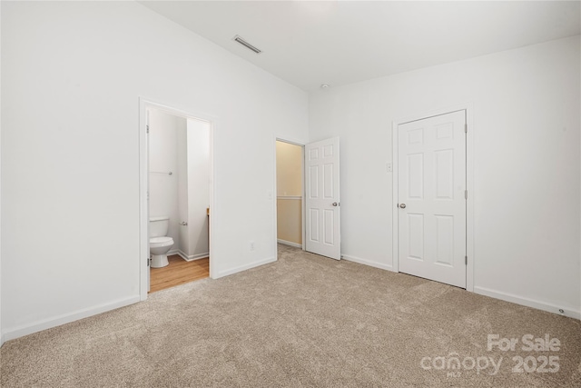 unfurnished bedroom featuring a closet, light colored carpet, and ensuite bath