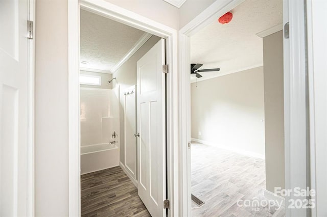 hall with wood-type flooring, a textured ceiling, and ornamental molding