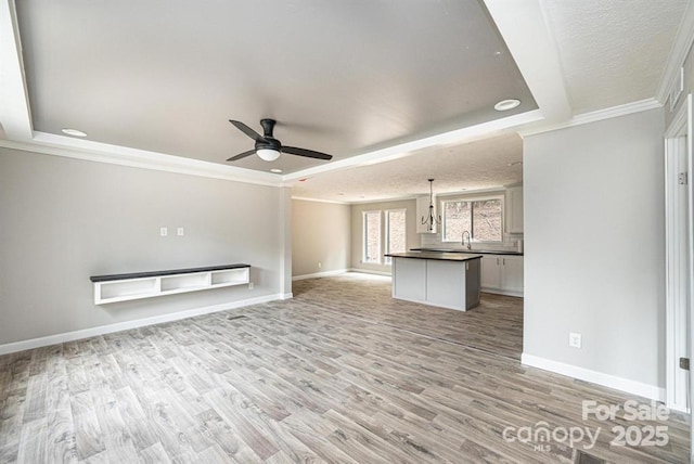 unfurnished living room with a tray ceiling, ceiling fan, sink, and light wood-type flooring