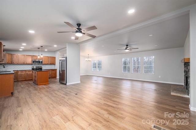 kitchen with stainless steel appliances, light hardwood / wood-style floors, a kitchen island, hanging light fixtures, and a stone fireplace