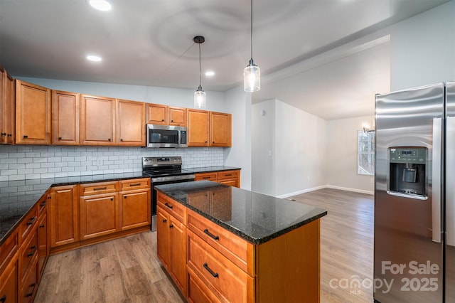 kitchen with backsplash, vaulted ceiling, dark stone countertops, decorative light fixtures, and stainless steel appliances