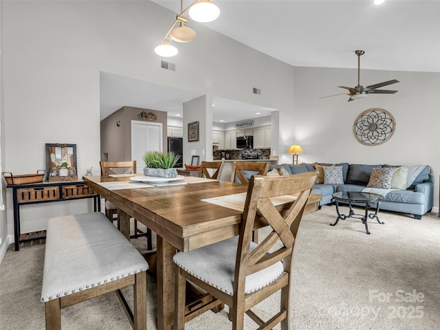 dining space featuring light carpet, ceiling fan, and high vaulted ceiling