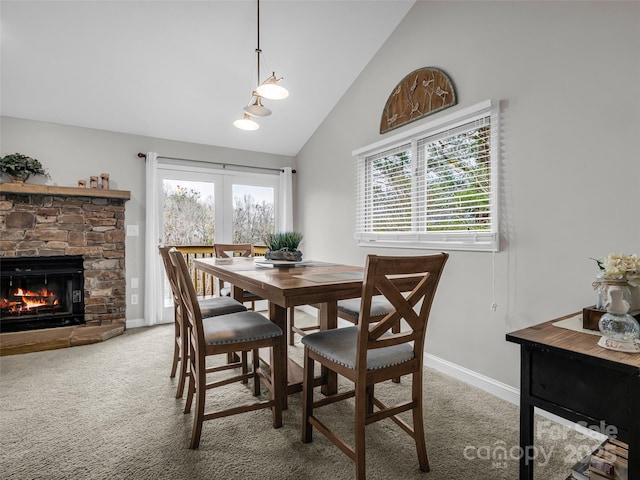 carpeted dining area with high vaulted ceiling and a stone fireplace