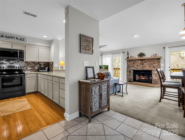 kitchen with backsplash, a stone fireplace, ceiling fan, light tile patterned floors, and stainless steel appliances