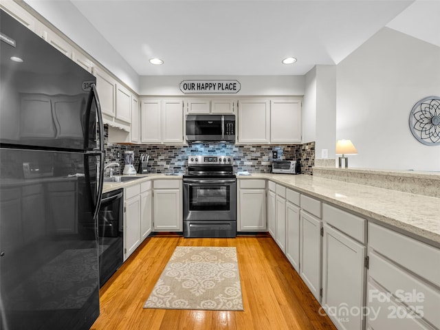 kitchen with backsplash, black appliances, white cabinets, light hardwood / wood-style flooring, and light stone counters