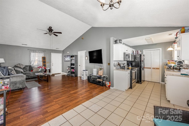 living room with light tile patterned floors, ceiling fan with notable chandelier, a textured ceiling, and high vaulted ceiling