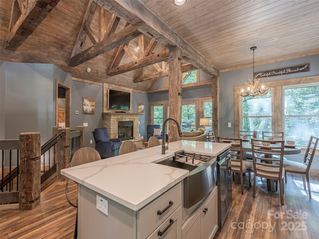 kitchen featuring hanging light fixtures, a stone fireplace, beamed ceiling, an island with sink, and wood ceiling