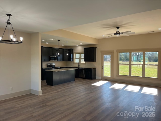 kitchen featuring ceiling fan with notable chandelier, stainless steel appliances, dark wood-type flooring, pendant lighting, and a center island