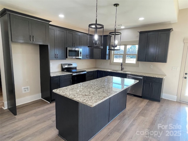 kitchen featuring hanging light fixtures, light hardwood / wood-style flooring, a kitchen island, light stone counters, and stainless steel appliances