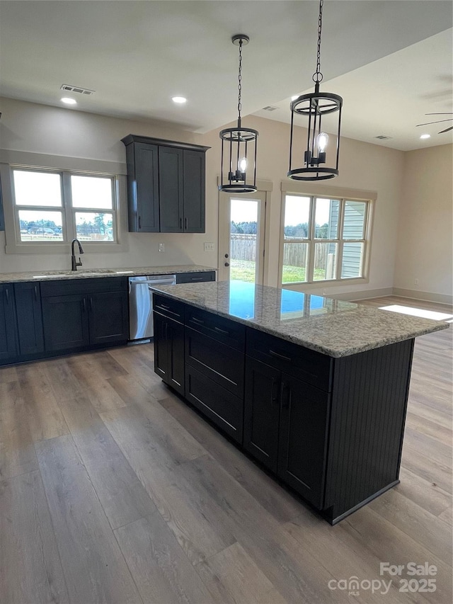 kitchen featuring stainless steel dishwasher, sink, light hardwood / wood-style flooring, a center island, and hanging light fixtures