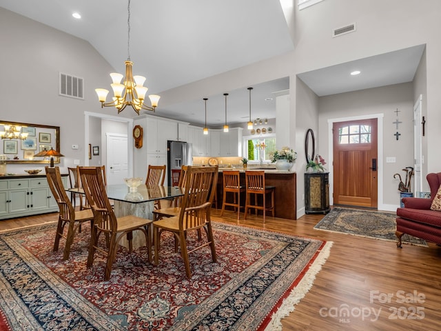 dining area with light wood-type flooring, high vaulted ceiling, and a chandelier