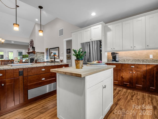 kitchen featuring backsplash, white cabinets, stainless steel refrigerator with ice dispenser, hanging light fixtures, and a kitchen island