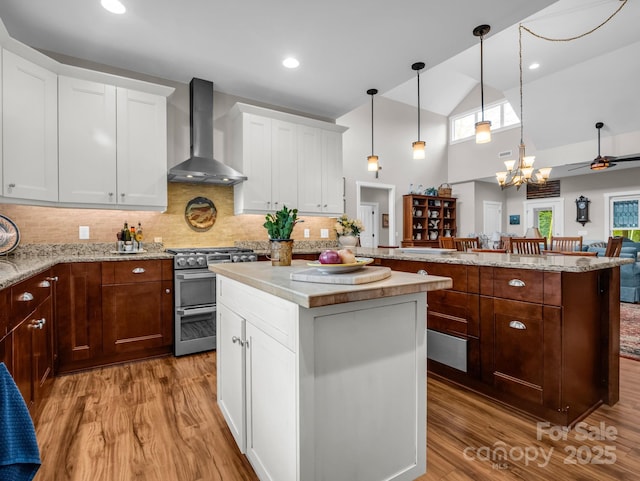 kitchen with a center island, decorative light fixtures, high end stainless steel range oven, and wall chimney range hood