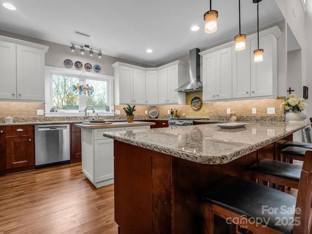 kitchen featuring wall chimney exhaust hood, hanging light fixtures, stainless steel appliances, a breakfast bar, and white cabinets