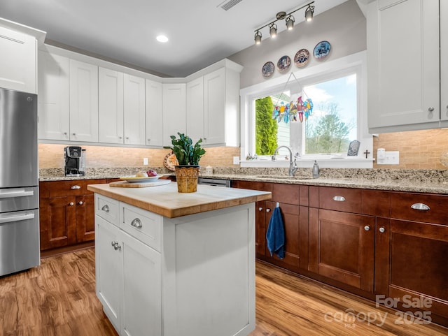 kitchen featuring sink, white cabinetry, light hardwood / wood-style floors, a kitchen island, and stainless steel refrigerator