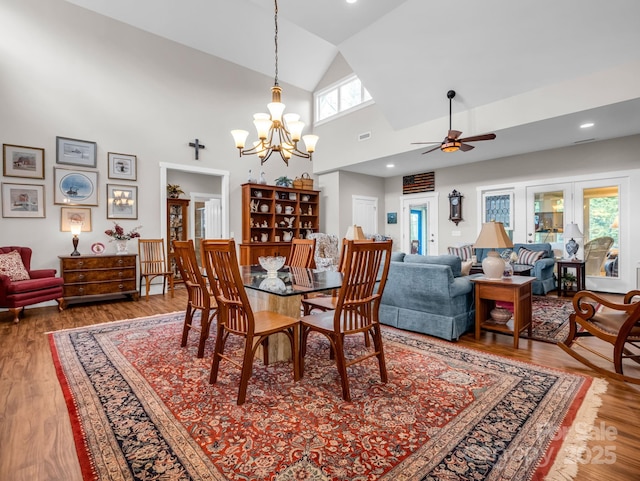 dining space with high vaulted ceiling, wood-type flooring, and ceiling fan with notable chandelier