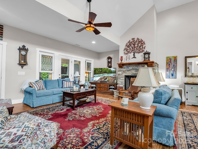 living room with a stone fireplace, ceiling fan, wood-type flooring, and vaulted ceiling