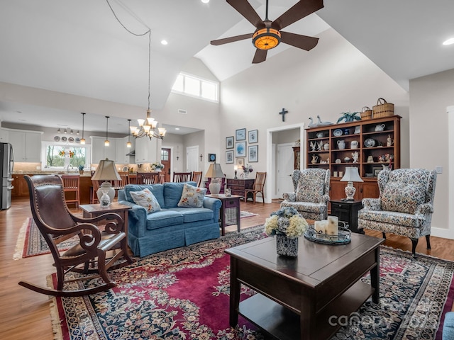 living room with high vaulted ceiling, light hardwood / wood-style floors, and ceiling fan with notable chandelier