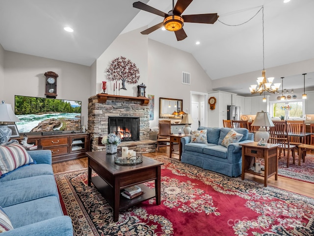 living room featuring a stone fireplace, hardwood / wood-style floors, high vaulted ceiling, and ceiling fan with notable chandelier