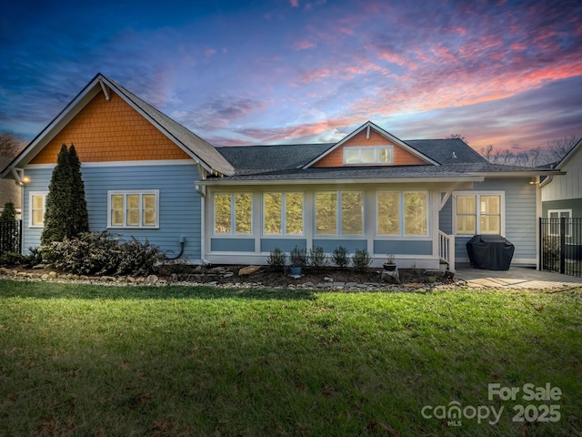 back house at dusk featuring a lawn, a patio area, and a sunroom