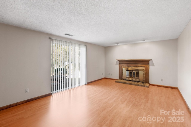 unfurnished living room with a brick fireplace, a textured ceiling, and light hardwood / wood-style flooring