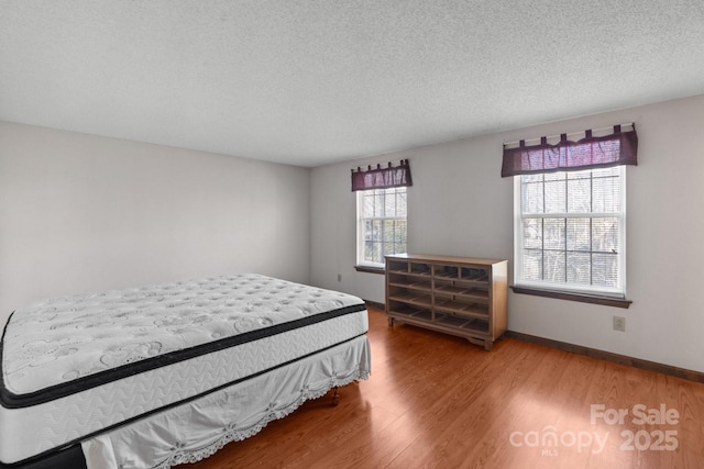 bedroom with a textured ceiling, multiple windows, and hardwood / wood-style flooring