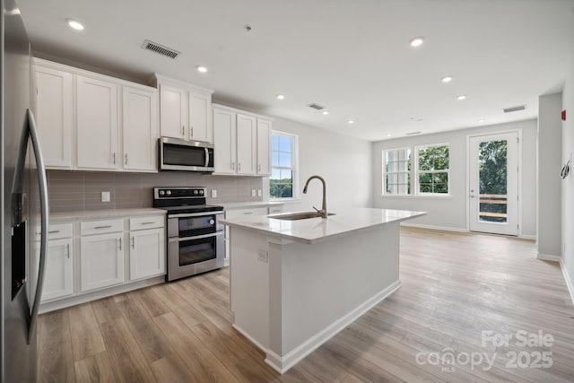 kitchen with a center island with sink, sink, appliances with stainless steel finishes, tasteful backsplash, and white cabinetry