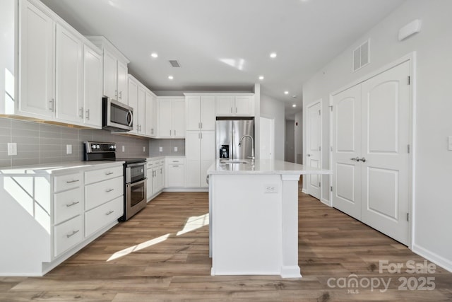 kitchen featuring hardwood / wood-style flooring, appliances with stainless steel finishes, a kitchen island with sink, and white cabinets