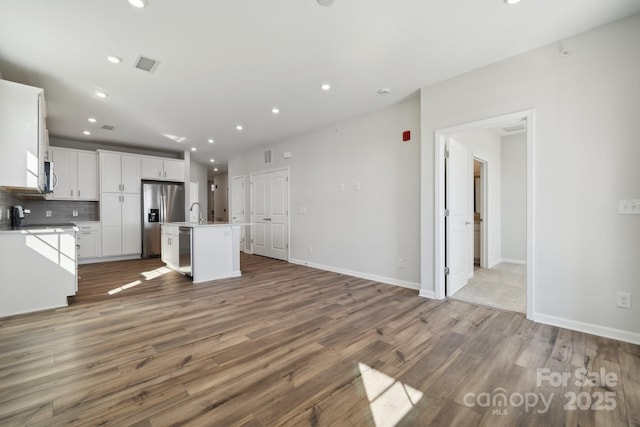 kitchen featuring appliances with stainless steel finishes, white cabinets, hardwood / wood-style flooring, a kitchen island with sink, and backsplash