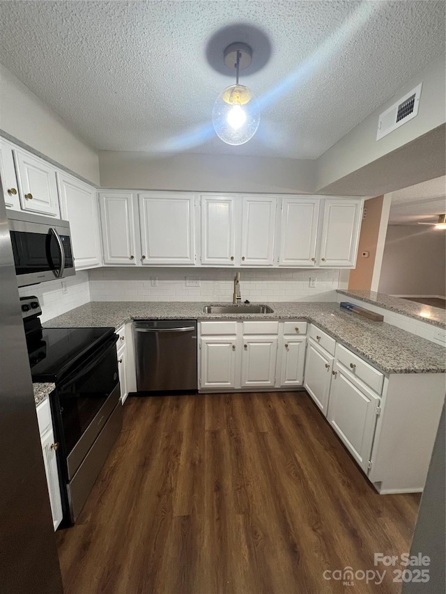 kitchen with kitchen peninsula, light stone counters, stainless steel appliances, sink, and white cabinetry