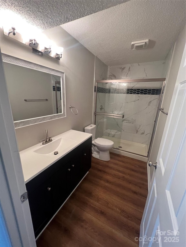 bathroom with an enclosed shower, vanity, a textured ceiling, hardwood / wood-style flooring, and toilet