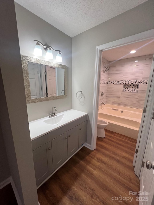 full bathroom featuring shower / bathing tub combination, hardwood / wood-style floors, a textured ceiling, toilet, and vanity