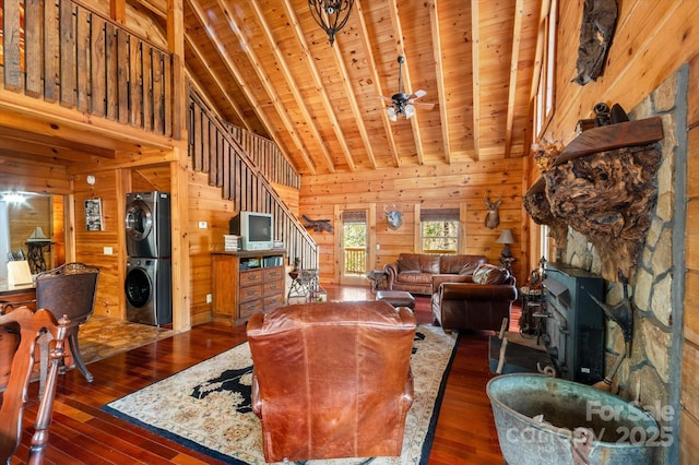 living room with wooden walls, dark wood-type flooring, high vaulted ceiling, stacked washer / dryer, and wooden ceiling