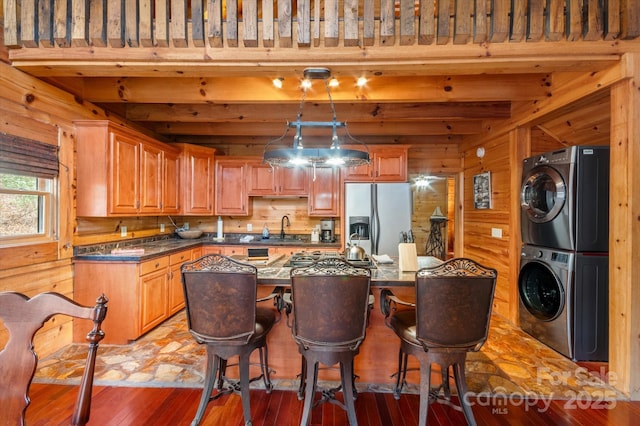 kitchen featuring stainless steel fridge, stacked washing maching and dryer, sink, wood-type flooring, and beam ceiling