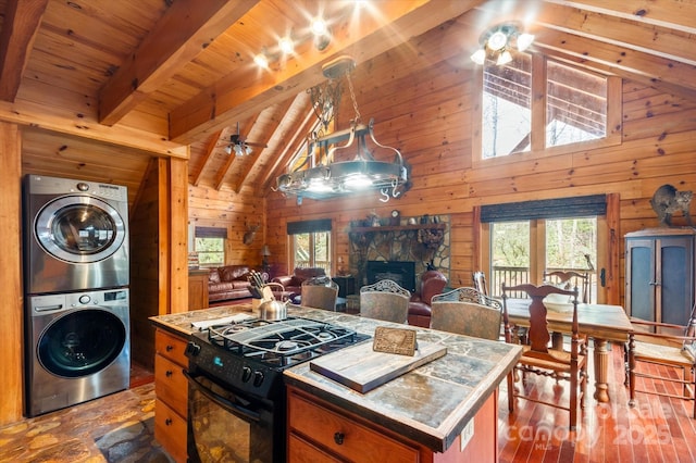 kitchen with black gas range, wood walls, stacked washing maching and dryer, a fireplace, and a kitchen island