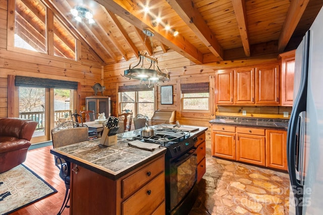 kitchen featuring black range with gas stovetop, wooden ceiling, beamed ceiling, a kitchen island, and fridge