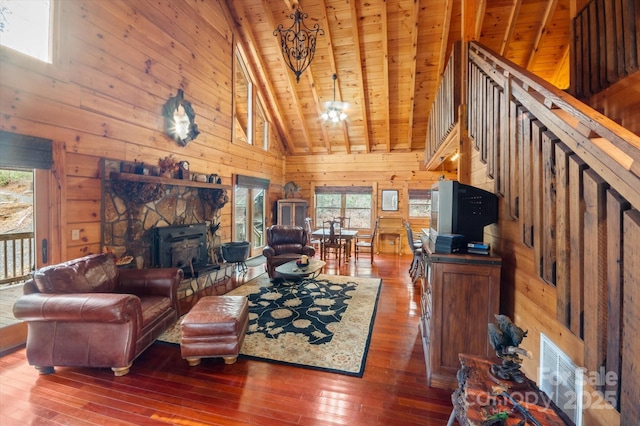 living room featuring beam ceiling, dark wood-type flooring, wooden ceiling, a stone fireplace, and a chandelier