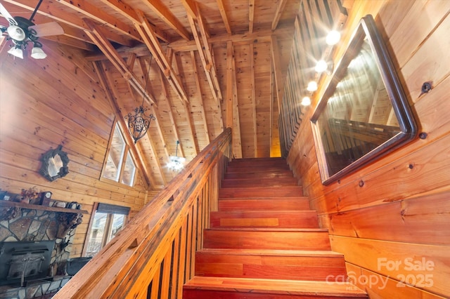 stairs with beam ceiling, wooden walls, a wood stove, and wooden ceiling